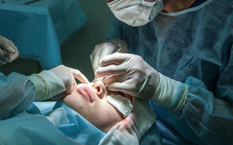 پزشک در اتاق عمل در حال جراحی زیبایی روی صورت دختری که بی هوش است