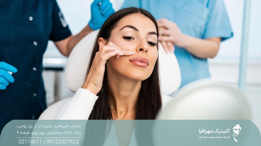 دختری که در یک کلینیک زیبایی نشسته است و صورت خود را در آینه می بیند و انگشت خود را بالای لب خود گذاشته است